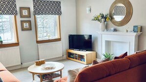 A living room with a sofa, a coffee table, a TV, a fireplace, and framed pictures on the wall. - Apartment 101 Kingsmills Road (Inverness)