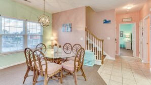 A dining area with a round glass table, six wicker chairs, a chandelier, and a view through large windows. - An Amazing Surfside Beach Escape (Surfside Beach)