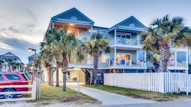 A beachfront residential building with multiple balconies, palm trees, and a gated driveway. - An Amazing Surfside Beach Escape (Surfside Beach)