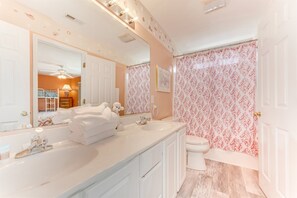 A bathroom with a double sink, a mirror, a toilet, and a shower curtain with a floral pattern.