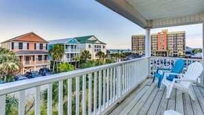 A balcony with white railings overlooking a beachfront area, featuring a row of parked cars and a building with a green roof. - An Amazing Surfside Beach Escape (Surfside Beach)