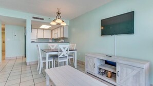 A modern kitchen with white cabinets, a dining table with chairs, a bench, and a TV mounted on the wall. - Atlantica Resort 751 (Myrtle Beach)