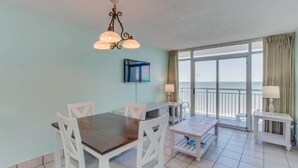 A dining area with a table and chairs, a TV, and a view of the ocean. - Atlantica Resort 751 (Myrtle Beach)