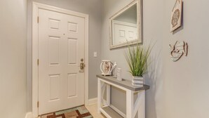 Um corredor com uma porta branca, um aparador com planta em vaso e detalhes decorativos nas paredes.