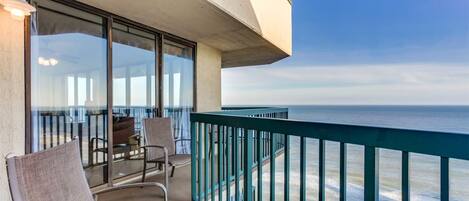A balcony with a view of the ocean, furnished with chairs and a table.