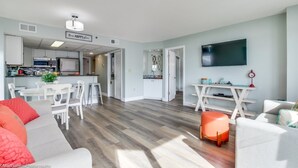 Ein modernes Wohnzimmer mit einem grauen Sofa, einem Essbereich mit weißen Stühlen und einer Küche im Hintergrund.