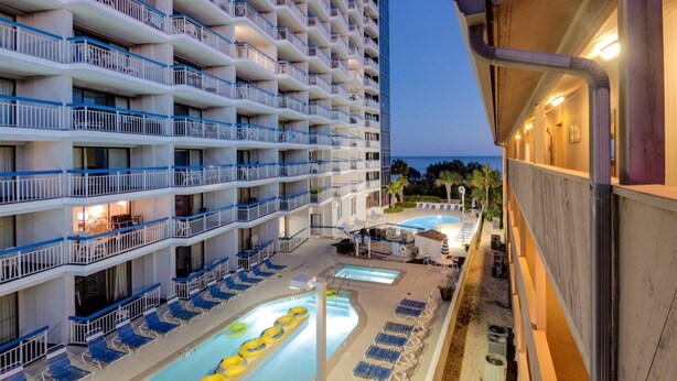 A multi-story hotel with balconies, a pool area with sun loungers, and a view of the ocean. - Forest Dunes 1501 Escape! (Myrtle Beach)