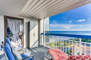 A balcony with a view of the ocean, a table with a red patterned tablecloth, and two blue chairs. - Forest Dunes 1501 Escape! (Myrtle Beach)