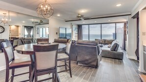 A spacious living area with a round dining table, leather seating, a large TV, and a view of the ocean. - Forest Dunes 1501 Escape! (Myrtle Beach)