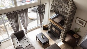 A living room with a stone fireplace, a sofa, a coffee table, and a view through large windows.