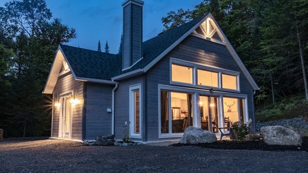A two-story house with a chimney, large windows, and a gravel driveway.