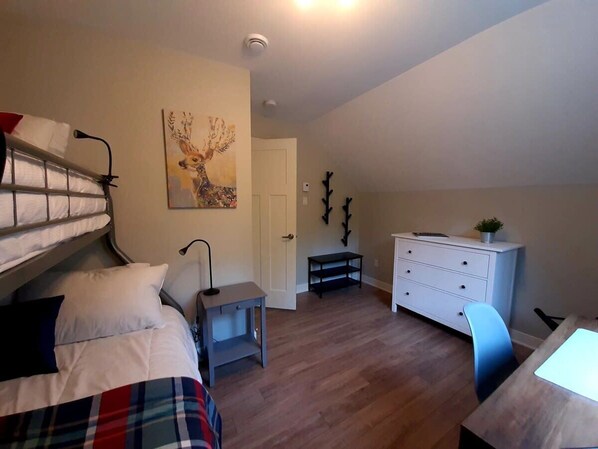 Un dormitorio con una cama litera, un escritorio, una silla, un aparador y un cuadro en la pared.