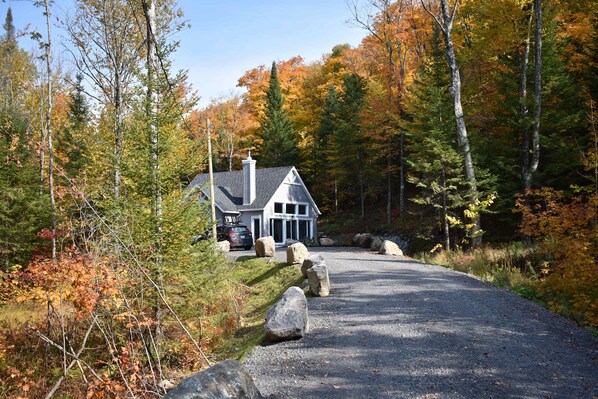 A house with a gravel driveway, surrounded by autumn-colored trees.
