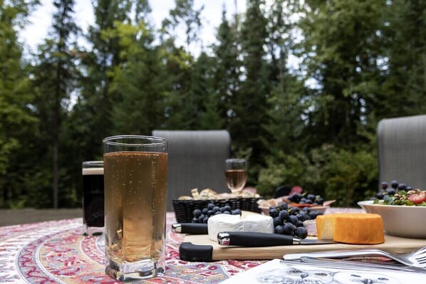 A table set outdoors with a glass of beer, cheese, grapes, and a bowl of salad.