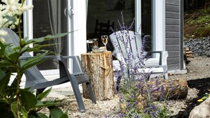 A cozy outdoor seating area with two chairs and a table, a wooden stump, and purple flowers.