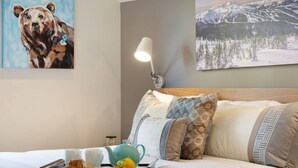 Hotelkamer met een bed, kussens, een dienblad met eten en een theepot, een schilderij van een beer en een berglandschap.
