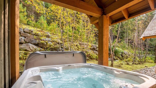 Een hottub in een houten prieel met uitzicht op een bebost gebied.