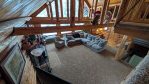 A cozy log cabin interior with a wooden ceiling, a gray sectional sofa, a fireplace, and a Christmas tree. - Sleeps 27, Dog Friendly, Fireplace, Ping Pong, Bumper Pool Table, Jetted tub (Fremont County)