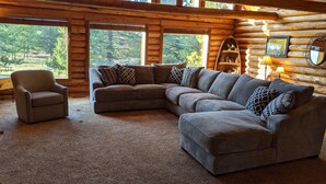 A log cabin interior with a sectional sofa, armchair, and a lamp. - Sleeps 27, Dog Friendly, Fireplace, Ping Pong, Bumper Pool Table, Jetted tub (Fremont County)