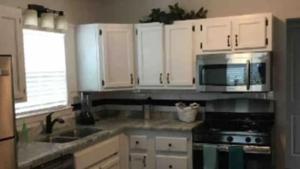 Una cucina compatta con mobili bianchi, un forno a microonde, un forno e una lavastoviglie.