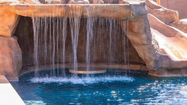 Een zwembad met een waterval, omringd door rotsformaties.