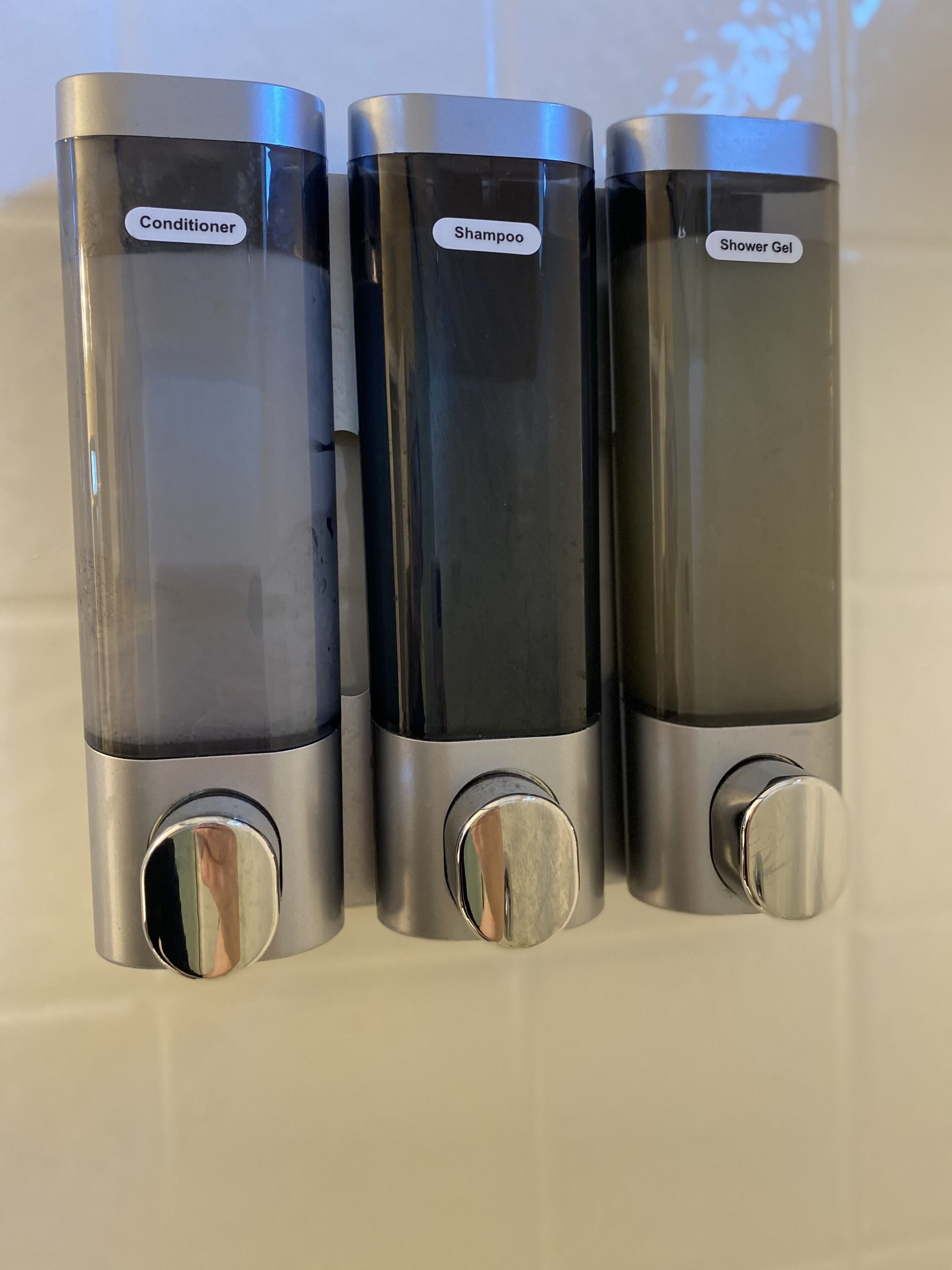 Trois récipients cylindriques étiquetés « Après-shampoing », « Shampoing » et « Gel douche ».