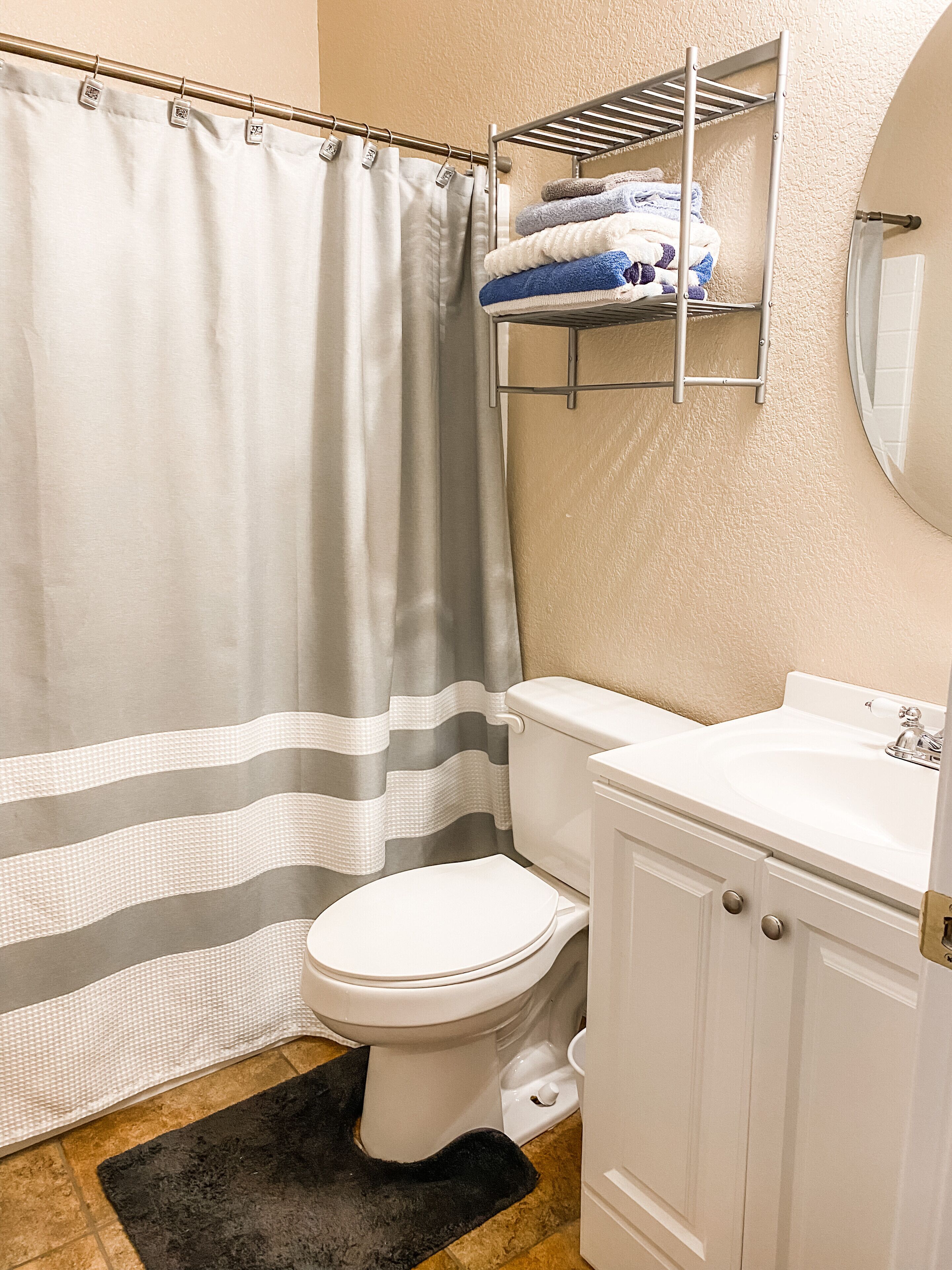 A bathroom with a shower curtain, a toilet, a sink, and a towel rack with towels.