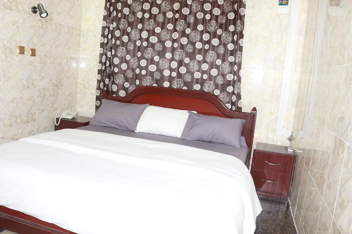 A neatly made bed with a white and gray duvet, a wooden headboard, and a brown and white polka dot curtain.