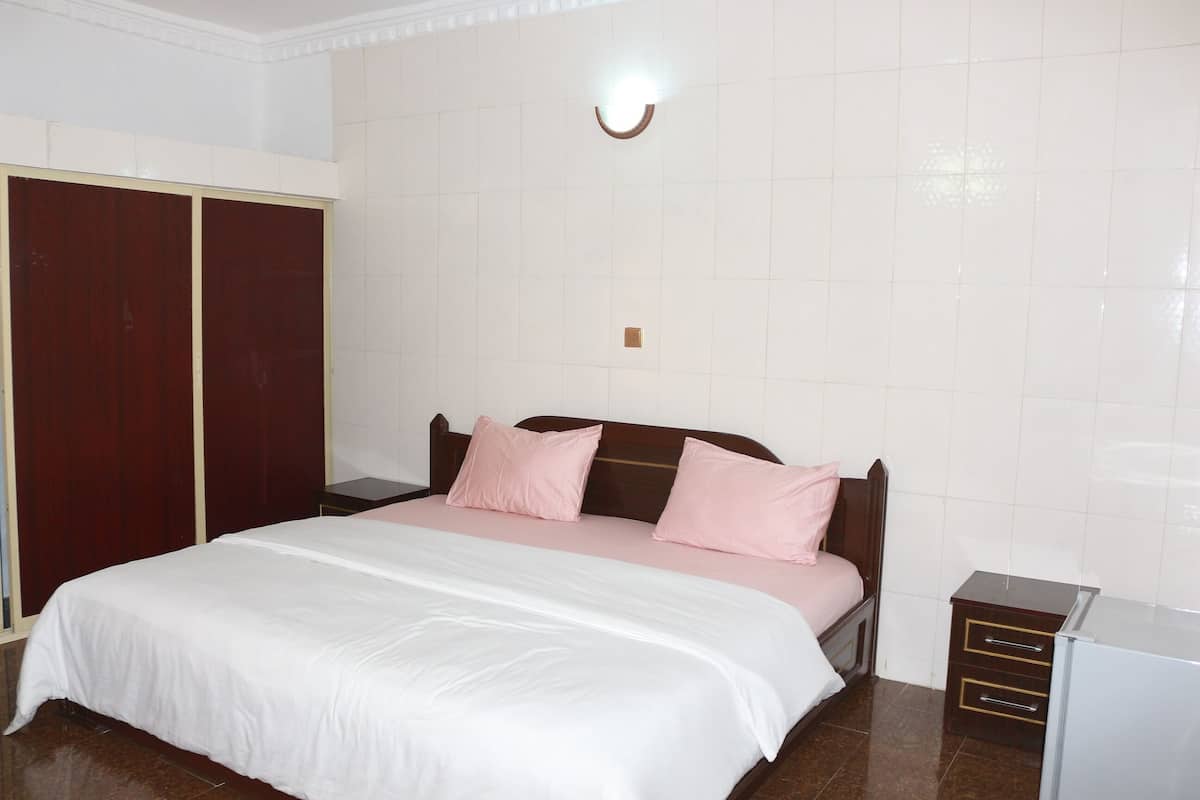 A bedroom with a bed, a wardrobe, a nightstand, and a wall-mounted light fixture.