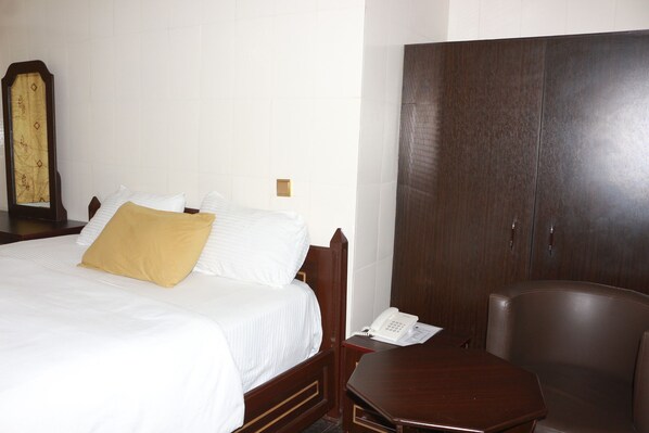 Una habitación de hotel con una cama, un armario de madera, un escritorio con teléfono y una silla.