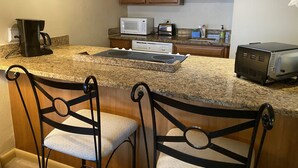 Eine Küche mit Granit Arbeitsplatten, integriertem Mikrowellenherd, Toaster und Kaffeemaschine. Zwei Barhocker mit gepolsterten Sitzen sind vorhanden.
