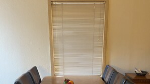 Ein Esstisch mit sechs Stühlen, einer Obstschale und einem Fenster mit Jalousien.