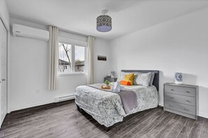 Un dormitorio con cama, mesita de noche, cómoda, ventana con cortinas e iluminación en el techo.