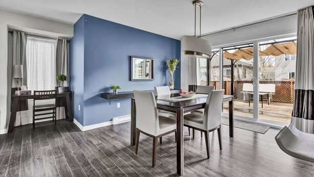 A modern dining area with a blue accent wall, a dining table with chairs, and a view of the outdoor patio.