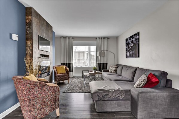 Una sala de estar moderna con un sofá gris, un sillón estampado y una mesa de centro.