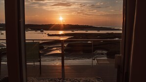 A sunset view from a room with a wooden deck overlooking a body of water with boats.