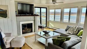 A living room with a fireplace, a television, a sofa, and large windows with a view of the water.