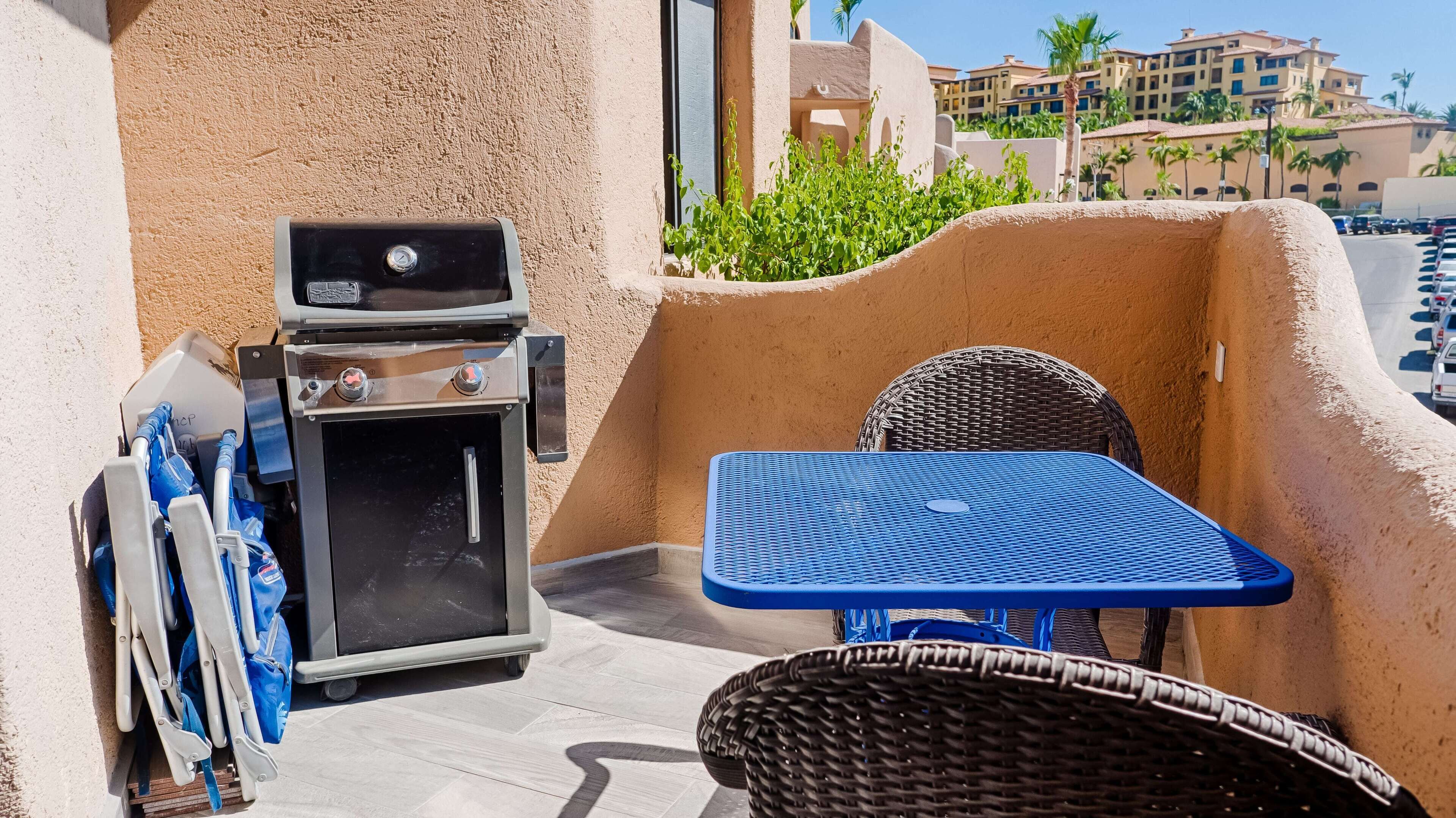 Een balkon met een barbecue, een tafel en stoelen.