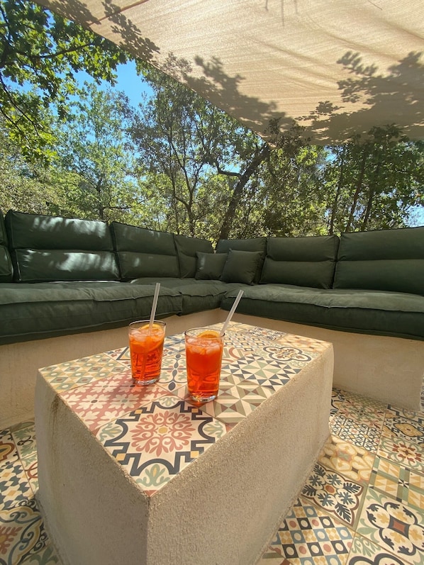 A patio area with a patterned table, two drinks, and a green sofa under a shaded area.