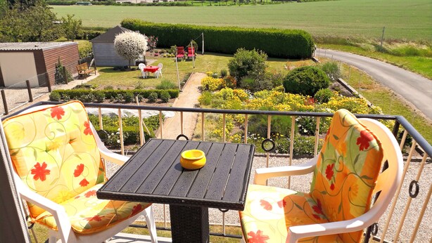 A balcony with two chairs and a table, overlooking a garden with a hedge, flowers, and a road. - Vacation apartment Am Damm with a direct view of the Rhine DTV 4 stars (Wesel)