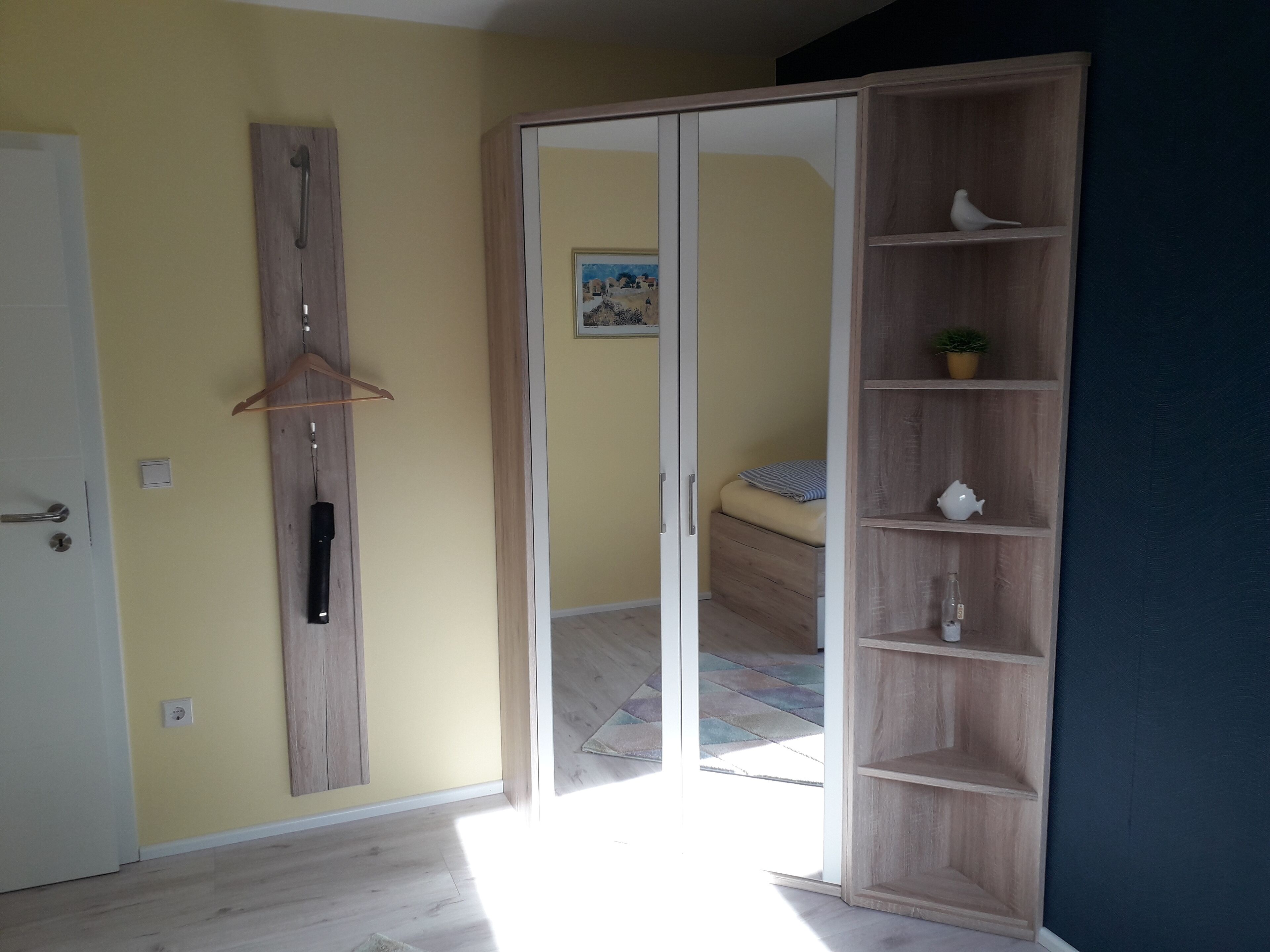 Een kamer met een houten garderobe, een bed met een gestreept kussen en een klein plankje met een plant en decoratieve object.