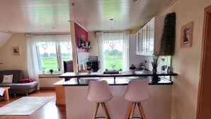 A modern kitchen with a central island, two bar stools, and a view of a green landscape through large windows. - Vacation apartment Am Damm with a direct view of the Rhine DTV 4 stars (Wesel)