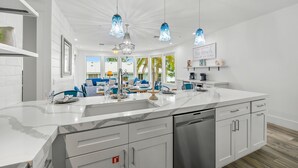 A modern kitchen with white cabinetry, a marble countertop, and pendant lights. - Beachfront Condo! Gulf Views, Pool, and Balcony (Holmes Beach)