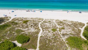 A beach with clear turquoise waters, sandy shore, and sparse vegetation. - Beachfront Condo! Gulf Views, Pool, and Balcony (Holmes Beach)