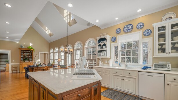 A spacious kitchen with a large island, white cabinetry, and a variety of decorative plates on the walls.