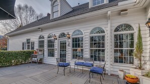 A white house with large arched windows, a wooden deck, and outdoor seating.
