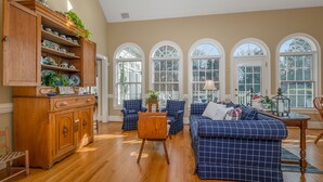 A spacious living room with a wooden cabinet, blue checkered sofa, and a dining area with a table and chairs.