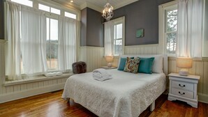 Un dormitorio con una cama grande, cortinas blancas, una lámpara de araña y vistas al exterior.