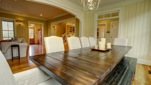 Un comedor amplio con una gran mesa de madera, sillas blancas tapizadas y una araña.