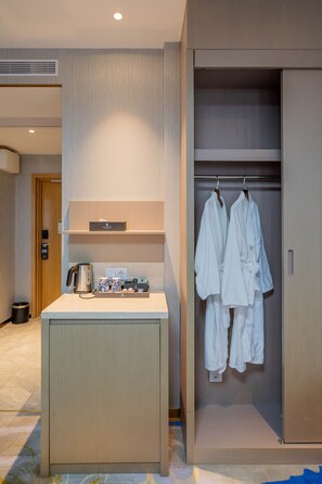 A hotel room with a minibar, a robe rack, and a wooden door. - Livington Hotel (Vallingby)